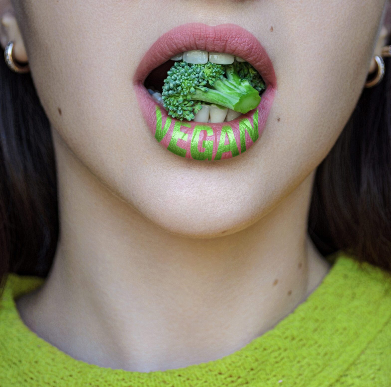 A close-up of a person's open mouth filled with broccoli, with the word "vegan" written on their lips to market to non-vegans.