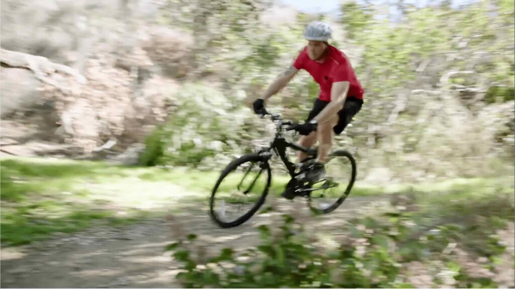 A person wearing a red shirt and helmet rides a mountain bike on a forest trail, showcasing the importance of outdoor activities in Medical Device marketing.
