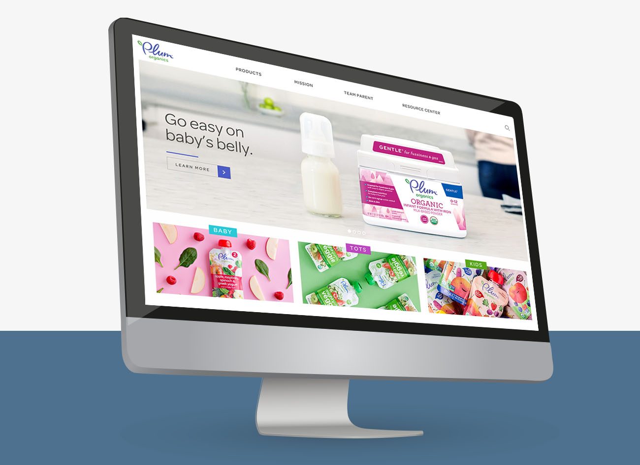 A computer monitor displays the Plum Organics website, focusing on a social media campaign with the headline, "Go easy on baby’s belly." The screen showcases colorful product images in pouches and jars, reflecting the unvarnished truth of real parenting.