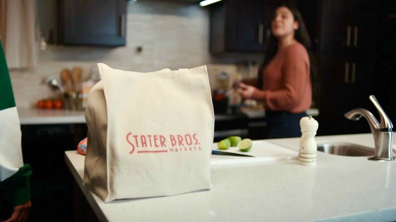 A grocery bag from Stater Bros Markets sits on a kitchen counter, while a woman in the background prepares food, demonstrating effective content marketing in action.