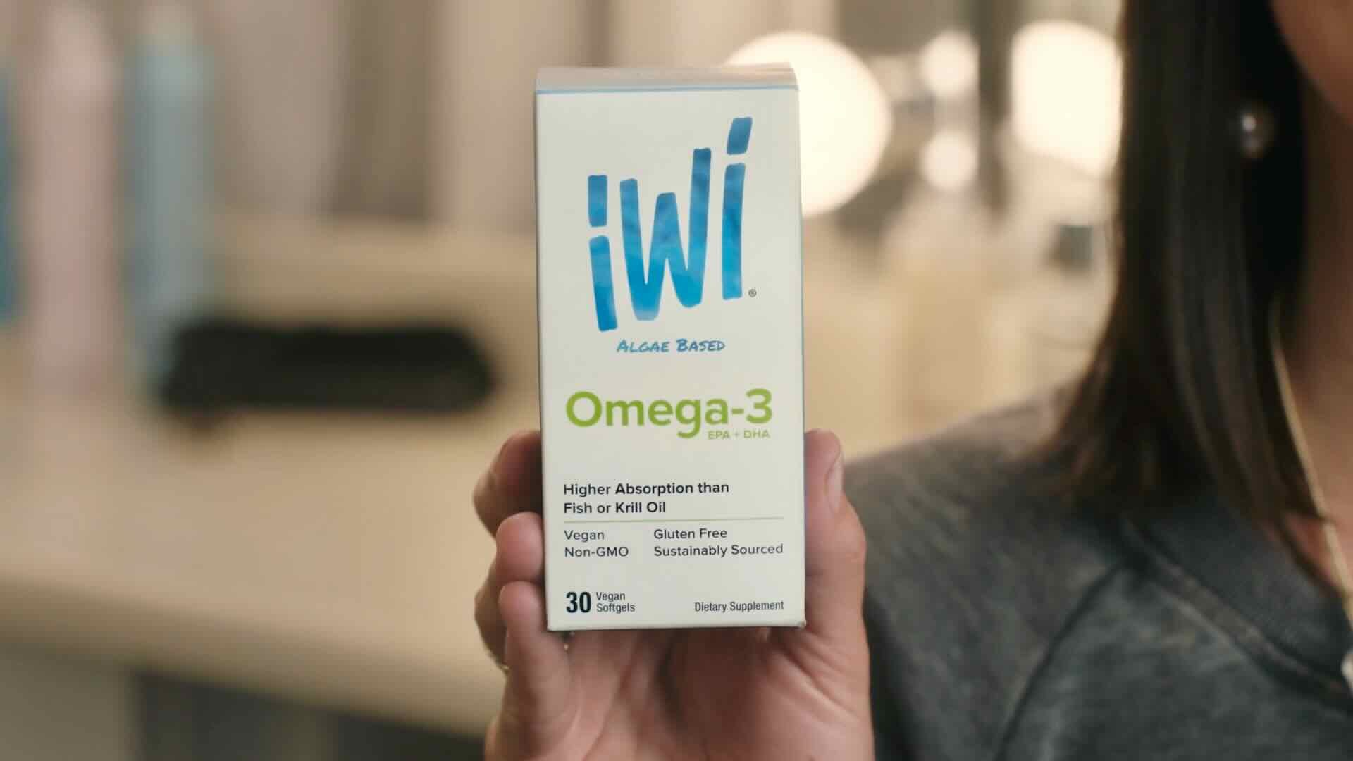 A person holds a box of iWi Omega-3 dietary supplements. The box states it is algae-based, higher absorption than fish or krill oil, vegan, non-GMO, gluten-free, sustainably sourced with 30 soft gels. Discover the seaweed benefits in these supplements for overall health.