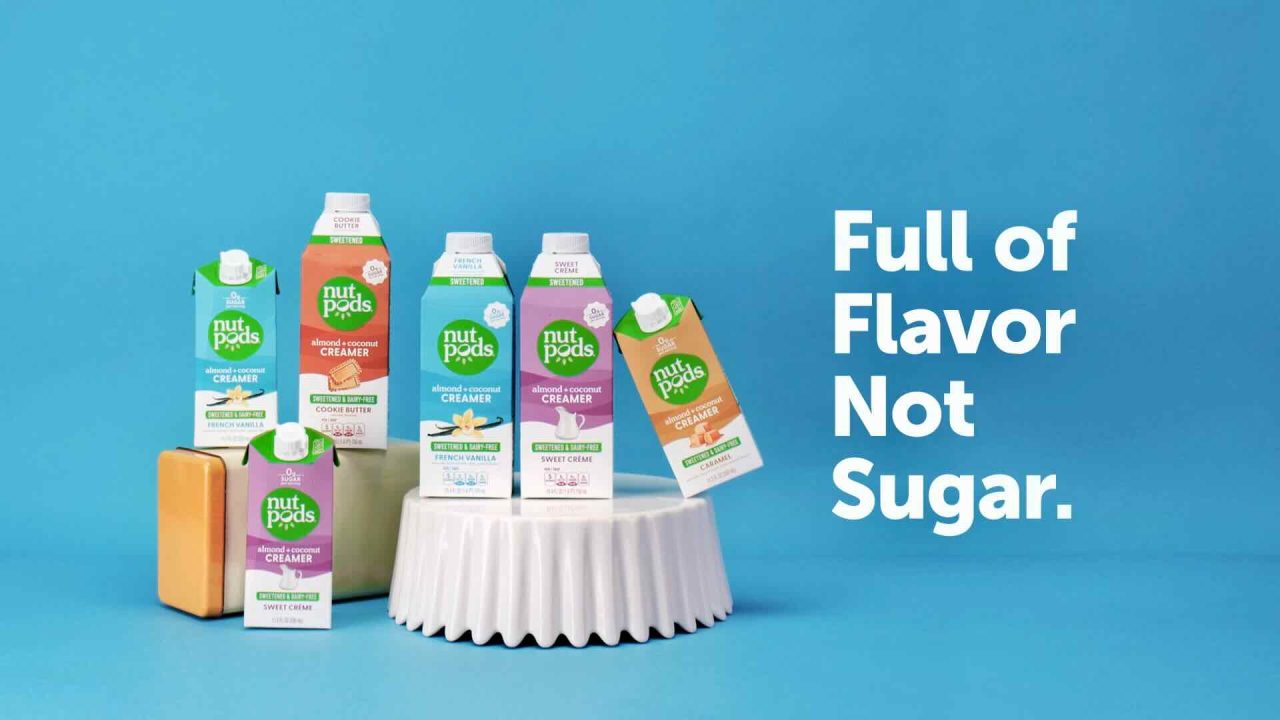 Six Nutpods creamer cartons arranged with various flavors, set against a blue background. Text to the right reads "Full of Flavor, Not Sugar." Perfect for content marketing that highlights healthy choices.